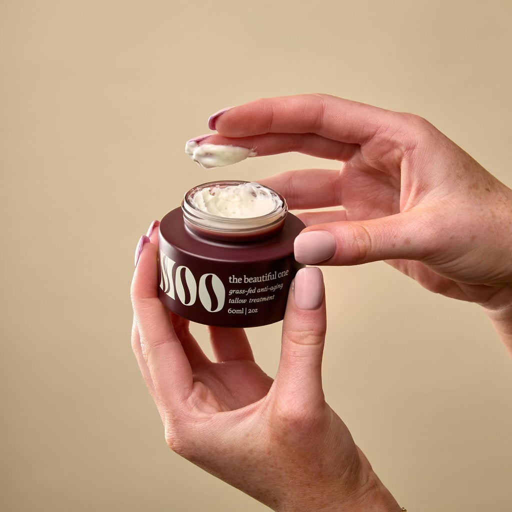 Close-up of The Beautiful One moisturizer being dipped into, showcasing its rich texture and natural ingredients including grass-fed suet tallow, organic baobab oil infused with gotu kola, organic plantain, and grass-fed bovine colostrum powder.