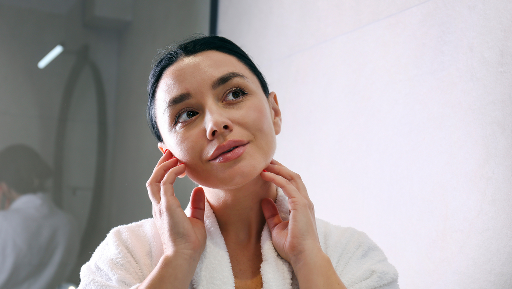 Young woman examining her skin in the mirror, highlighting the impact of advanced glycation end products (AGEs) on skin health and aging.