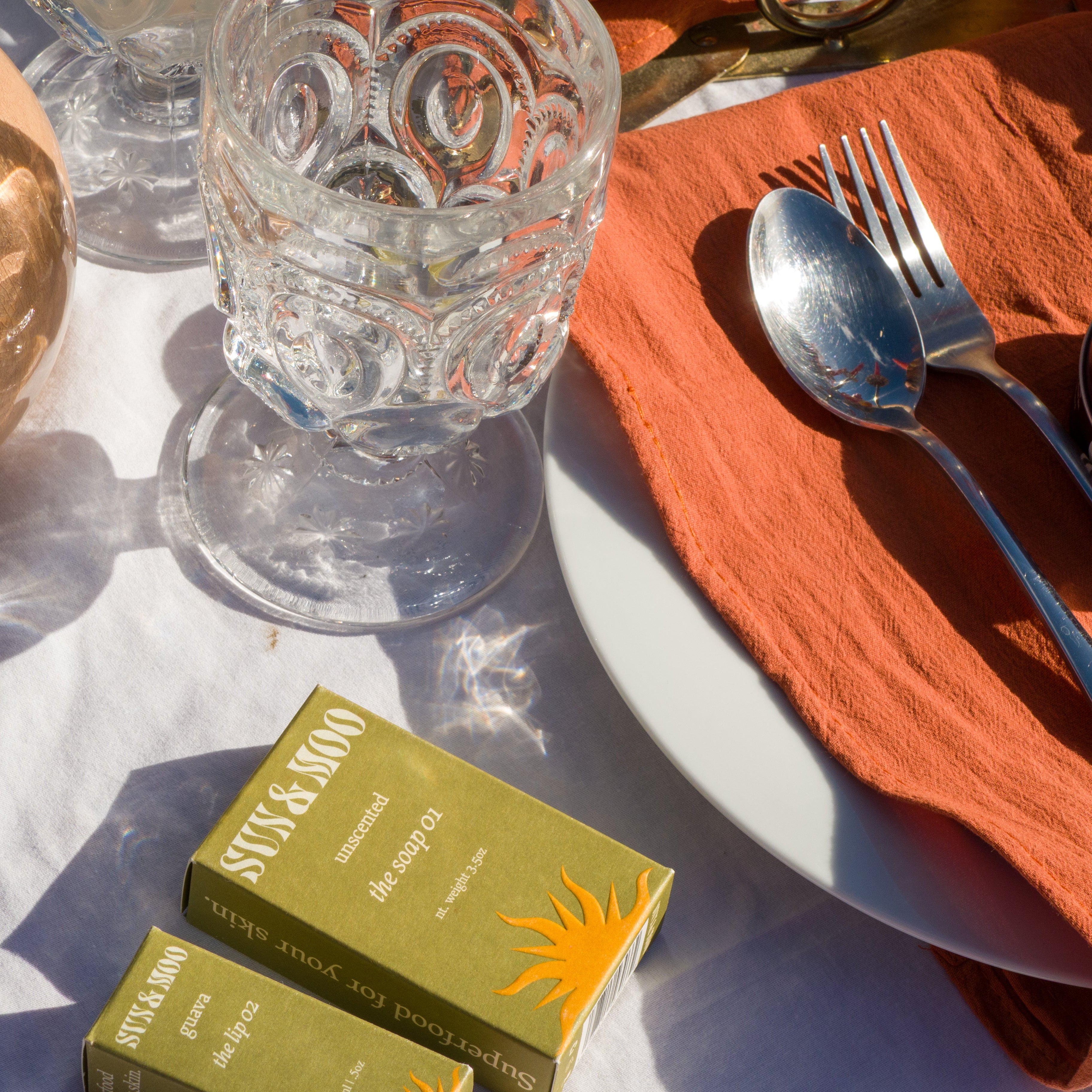 Table setting with orange napkin, silverware, and two boxes of Stik & Moos on a white tablecloth.