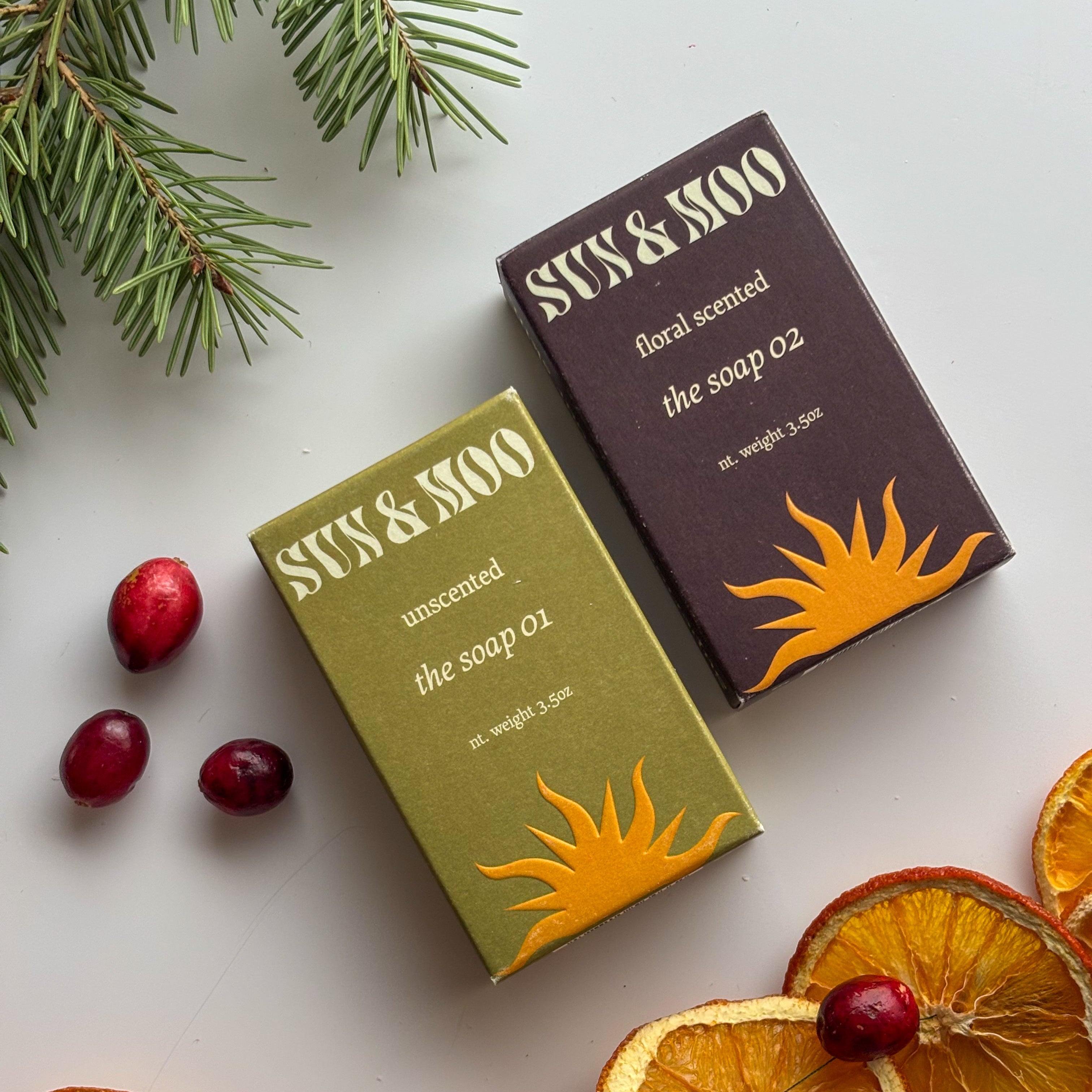 Two soap boxes from Sun & Mo'o with cranberries and orange slices on a light background
